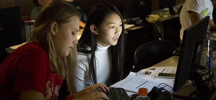 two students viewing monitor inside darkened classroom