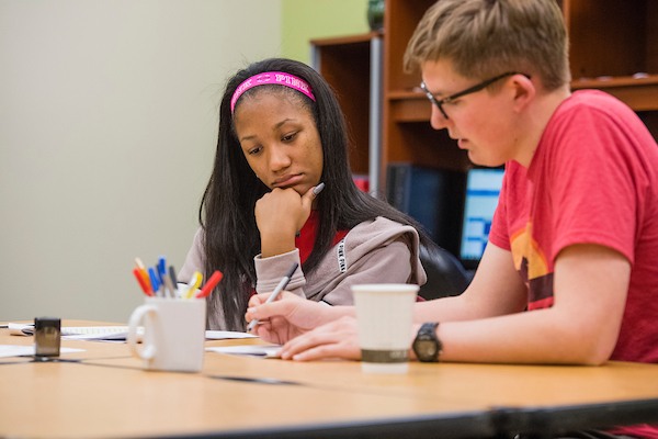 A male and female student sitting at table working on a paper together.
