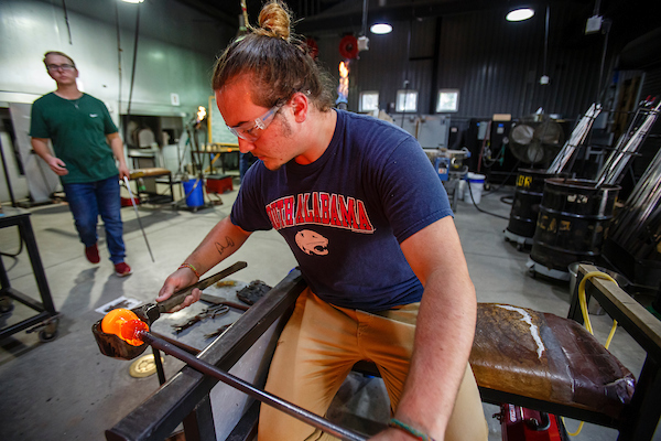 Male student working on glass blowing in art studio.