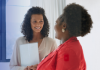 Two people smiling and talking holding a clipboard.