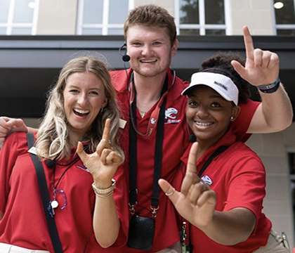 Three orientation leaders holding up J sign outside of campus housing.
