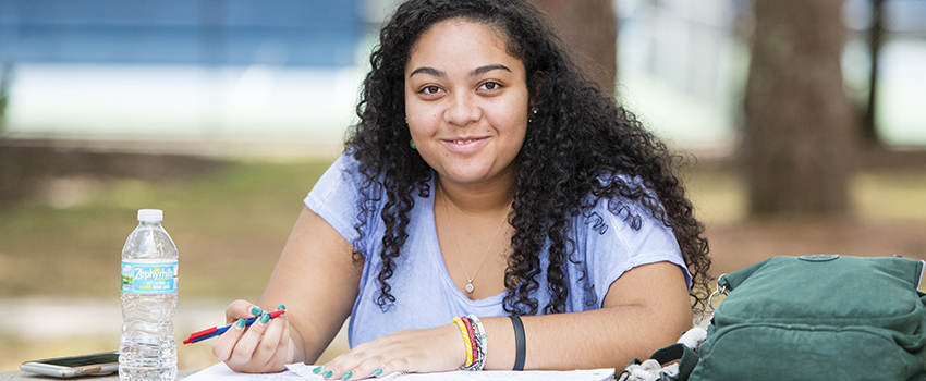 Female student smiling writing at a table outside.