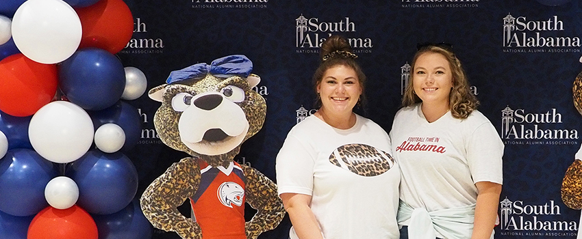 Two alumni members wearing South shirts standing next to Ms. Pawla cutout.