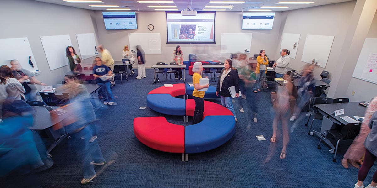 A group of people in a room with monitors and a s shaped seat.