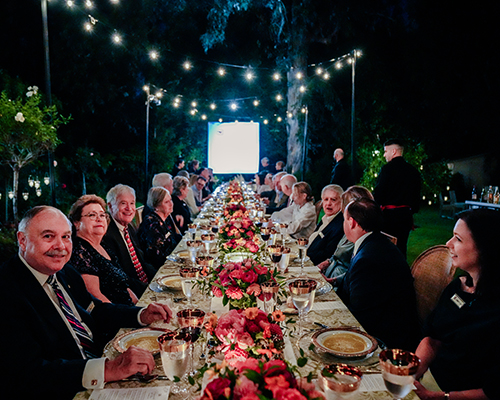 Alumni at dinner table under the night sky.