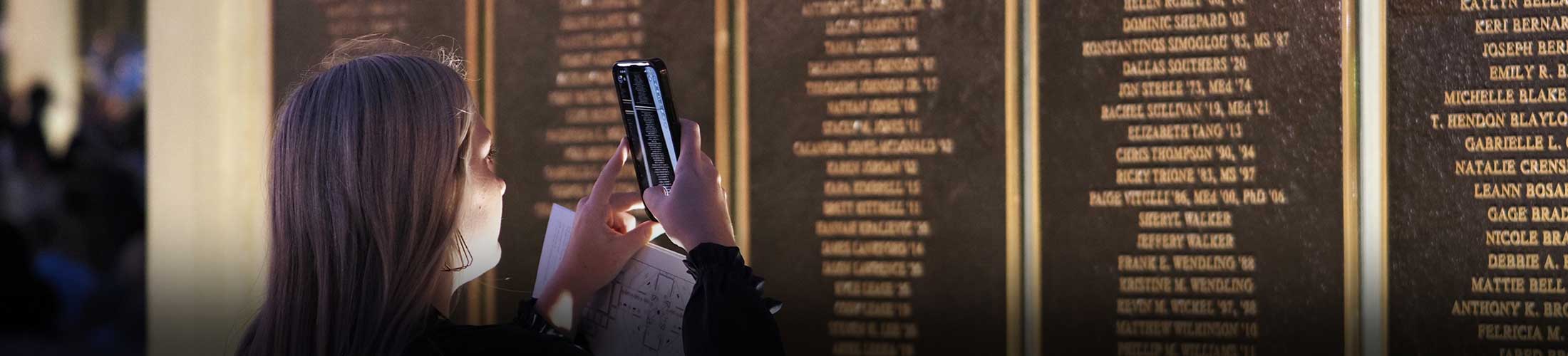 Alumni member taking picture of their name on the Wall of Honor.
