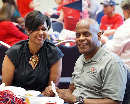 Alumni sitting at table eating at tailgating event at MacQueen Alumni Center.