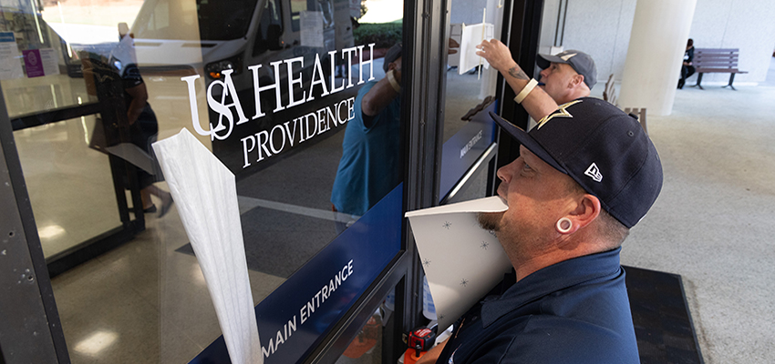 Two workers putting up USA Health signs at Providence Hospital.