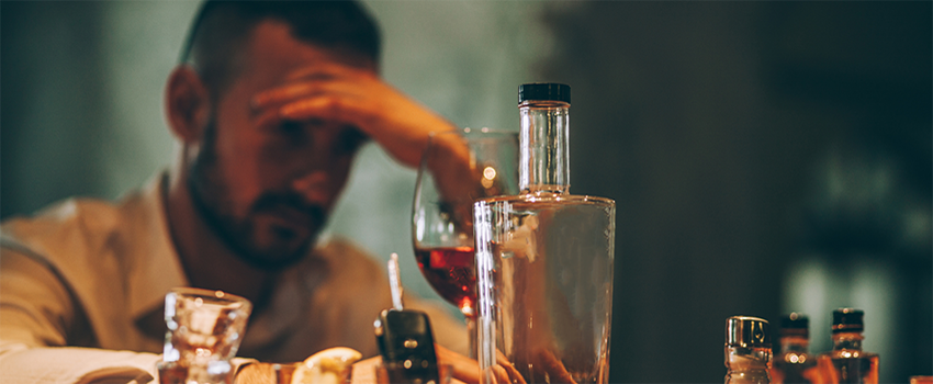 Person looks upset with head down with alcohol bottles sitting around him.