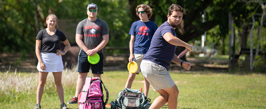 Students playing disc golf on campus with club sports.