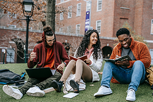 Three students looking at notebooks sitting outside on campus.