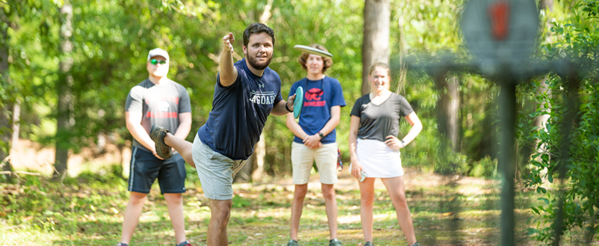 A male student throwing a disc with group of students playing disc golf at USA.