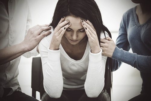 Woman looks depressed with people around her trying to help.