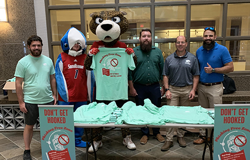 David Furman, Brandon Morris, and Cody Lawson standing with Southpaw, students, and shark at the table for Cyber Security Week.