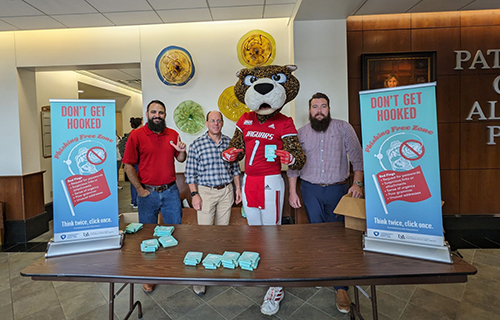 David Furman, Brandon Morris, and Cody Lawson standing with Southpaw at the table for Cyber Security Week.