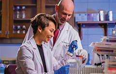 Man and woman working in lab in white coats looking at beakers.