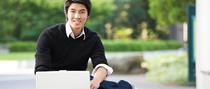 Man outside with laptop smiling.