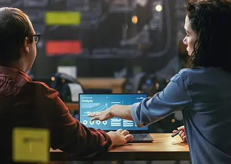 Two people working at table pointing to laptop.