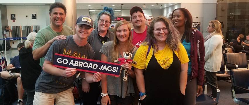 students standing together in an airport terminal holding a "go abroad jags" banner