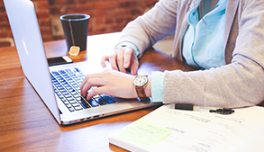 Person typing on laptop at table with tea