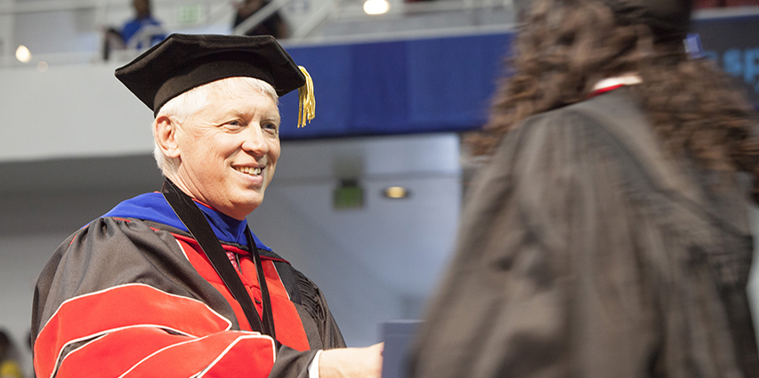 President Waldrop shaking hand of graduate at graduation ceremony.