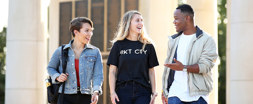 A male student and two female students smiling and talking walking outside on campus.