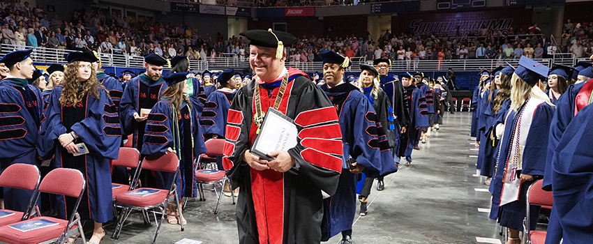 President Bonner walking into graduation in cap and gown.