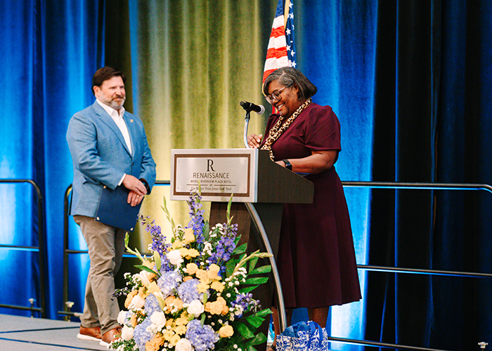 Woman at podium introduces man in blue suit jacket