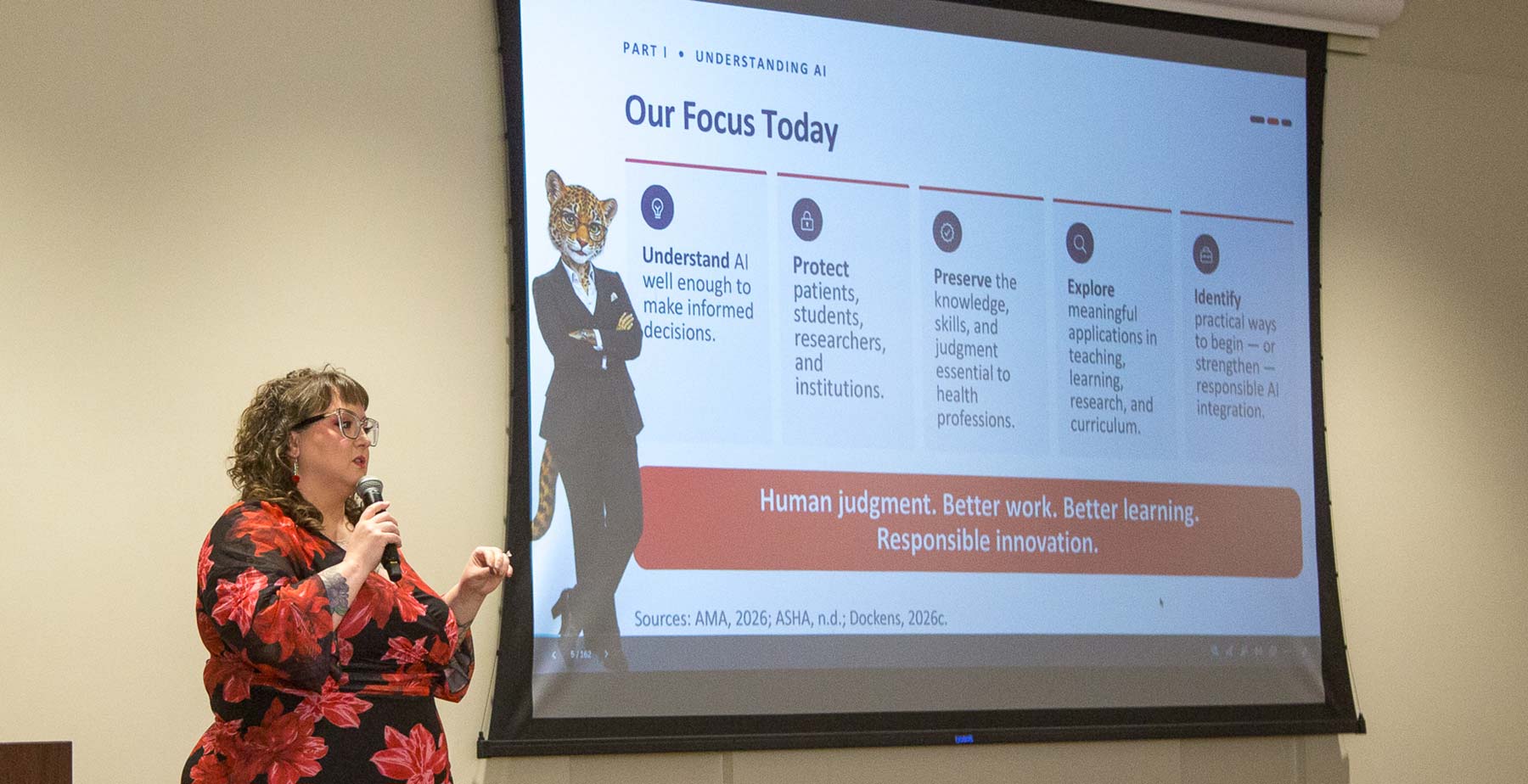 Dr. Ashley Dockens stands at a microphone presenting slides titled "Understanding AI" on a projection screen during a workshop for Allied Health faculty. data-lightbox='featured'