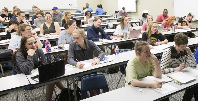 rows of students facing front of classroom - some with laptops open