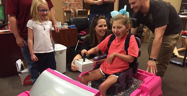 Emma Pablo takes a “sit test” in the toy vehicle USA’s Capstone Project team modified for her use. Assisting her are Michelle Jones, P.E., instrument engineer at Hargrove Engineers and Constructors, and Heath Skelton, one of the USA electrical engineering students.