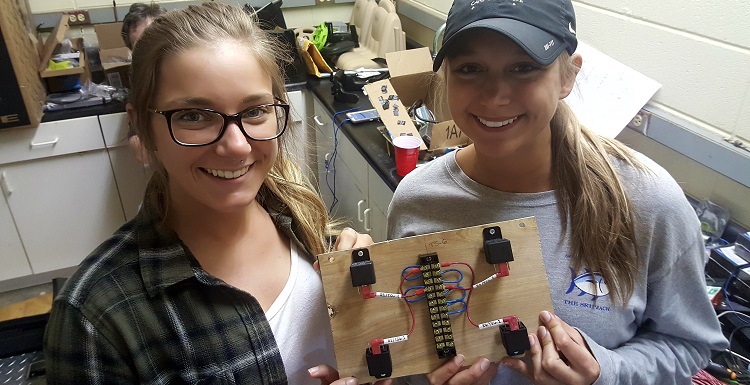 Electrical engineering students Victoria Antell, left, and Emaleigh Sargent were part of the USA Capstone Project team that modified a toy vehicle on behalf of a handicapped child. They’re holding a relay board used to reverse polarity for the wheel motors, which allows for forward and reverse drive direction.