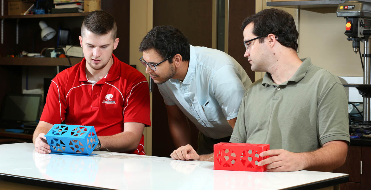 Graduate students Harrison White and Matthew Simmons flank Dr. Carlos Montalvo as they discuss the tradeoff from having two or more miniature satellites, called CubeSats, connected via a tether from an E-Sail. More CubeSats means more tethers and more thrust, but also more chances of tangling.  