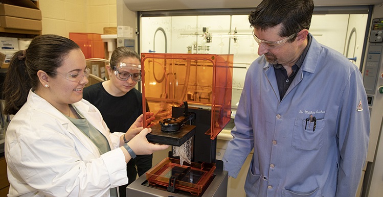 Senior chemistry students Madison McBroom, left, of Huntsville and Amanda Tanner of Cantonment, Fla., listen as Dr. William Richert talks about their research with ionic liquids in the field of 3D printing. 