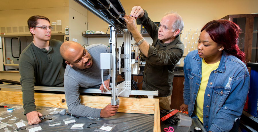 Electrical engineering senior Zack Peavy of Citronelle, mechanical engineering senior Kiante Evers of Gulfport, Miss., and computer engineering senior Ariel Pickett of Montgomery are adjusting the vertical travel distance of the robot head for a space station that will be used to grow crops in space. Assisting the students is Dr. Sam Russ, associate professor of electrical and computer engineering at the University of South Alabama.