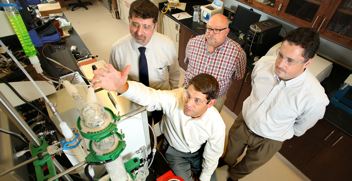 Dr. T. Grant Glover, seated, demonstrates an early-stage prototype of the next-generation carbon dioxide scrubber being developed for the International Space Station. Colleagues Dr. Matthew Reichert, from left, standing, Dr. James Davis and Dr. Kevin West are colleagues on the research project, which is financed by a $1.1 million grant from NASA. data-lightbox='featured'