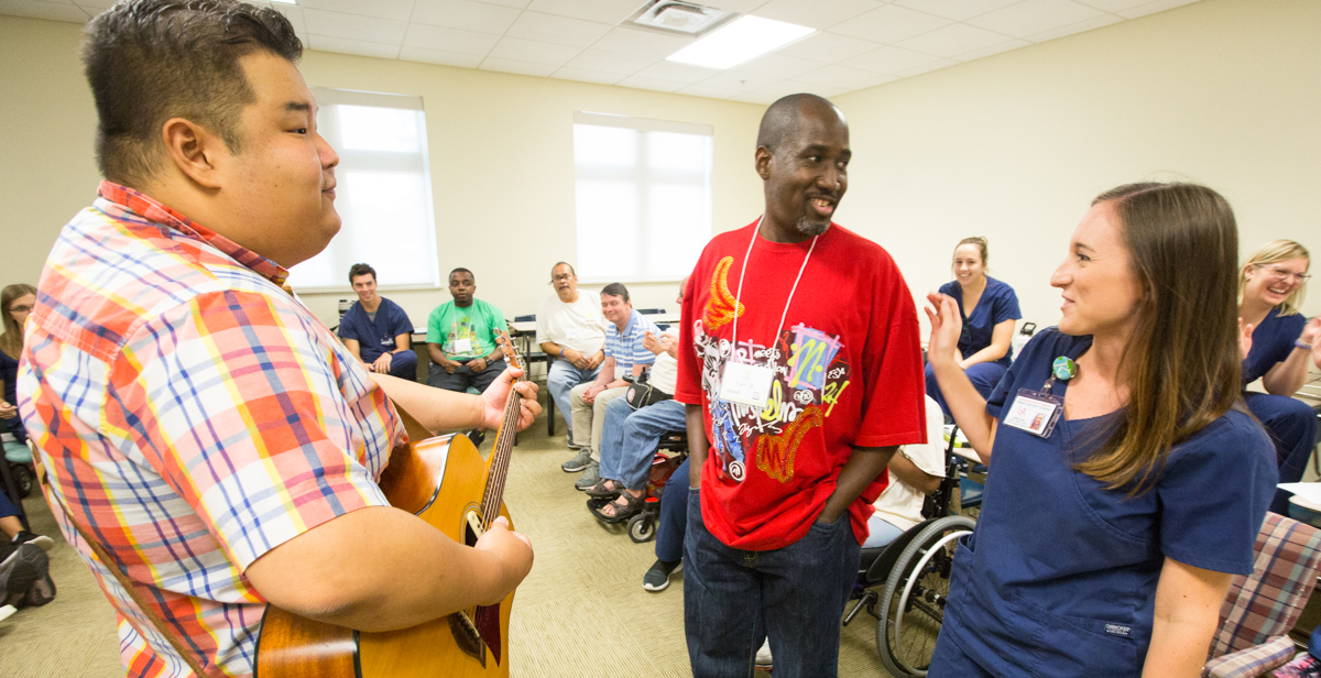 Kelsey Gross, University of South Alabama speech-language pathology graduate student, assists traumatic brain injury camp participant Larry Malone Jr., center, while music therapist Fred Ra leads Malone and other camp participants in creating a song using words suggested by the group.