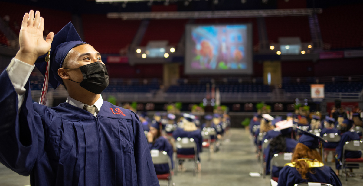 A 2021 College of Nursing graduate waves as he walks during spring commencement ceremony.