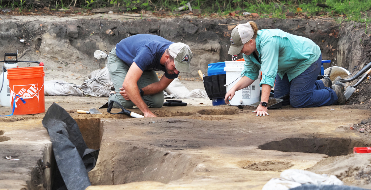 Emily Warner, left, with the USA Center for Archaeological Studies, and Thomas Grace, with Wiregrass Archaeological Consulting, bisect a feature in the soil at a dig site that is along the route for a proposed Mobile Bay bridge. After completing the excavation of half the feature, they will photograph and draw the profile, and then excavate the second half.