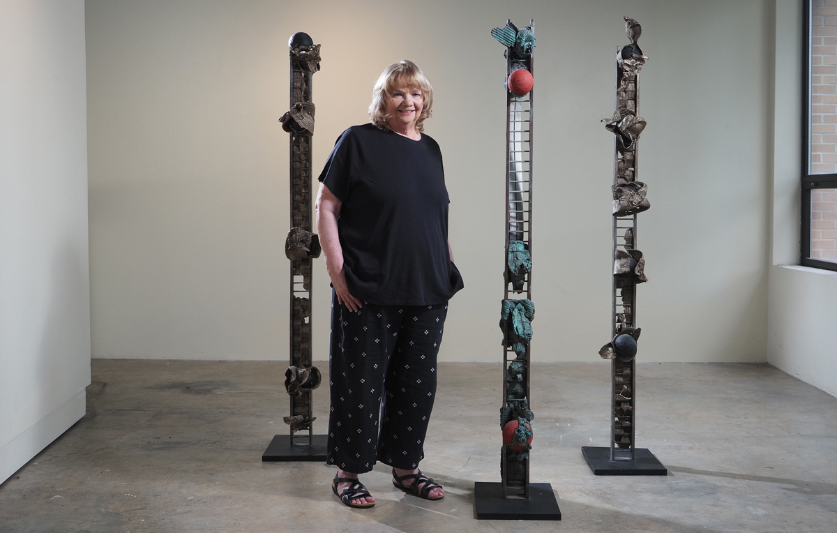 In a University of South Alabama gallery, Susan Fitzsimmons stands with a series of sculptures, "Sentinels and Guardians," which were inspired by the border wall with Mexico when she was teaching in McAllen, Texas. Two other sculptures by the chair of South's Department of Art and Art History will be featured in a Museum of Modern exhibit that opens this month.