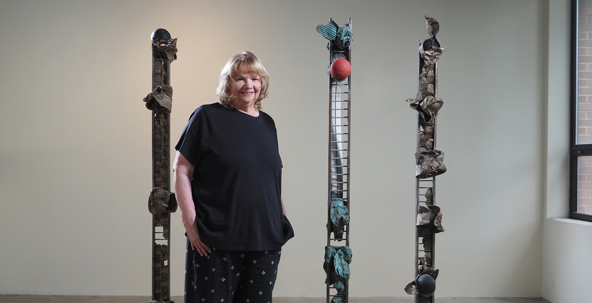 In a University of South Alabama gallery, Susan Fitzsimmons stands with a series of sculptures, "Sentinels and Guardians," which were inspired by the border wall with Mexico when she was teaching in McAllen, Texas. Two other sculptures by the chair of South's Department of Art and Art History will be featured in a Museum of Modern exhibit that opens this month.