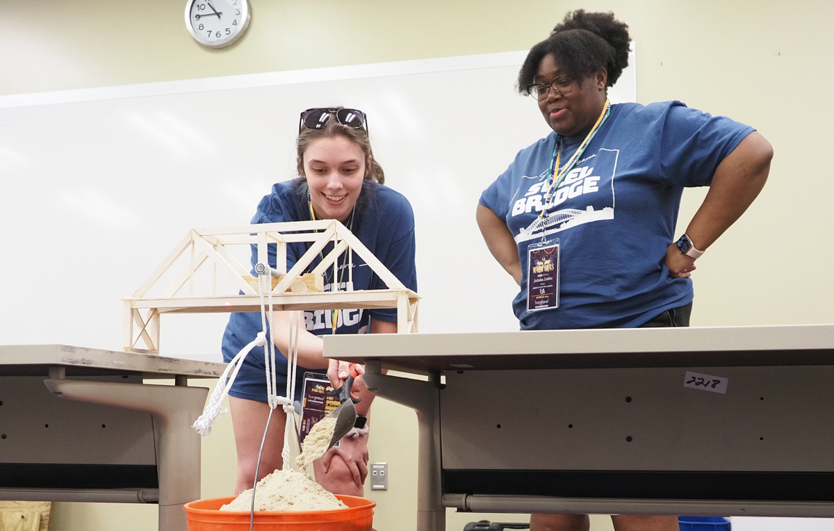 Katie Pruden, left, and Jalisha Littles add weight – carefully – to test the strength of South’s entry in the balsa wood bridge-building competition at the 2023 Gulf Coast Student Symposium, sponsored by the American Society of Civil Engineers.