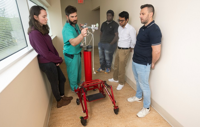 Engineering students, clockwise from left, Julia Nelson, Jalon McGhee, Ashwin Dahal and Joshua Neese visit with Dr. Tyler McDonald, in scrubs, to look at the mechanics of the walker used by Abby Flowers.