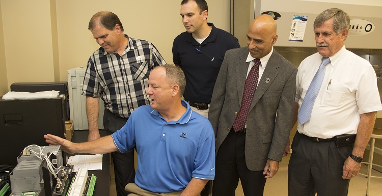 four individuals stand discussing Distributed Control System with Mark Damiani, seated, with Valero Energy and hardware on the left