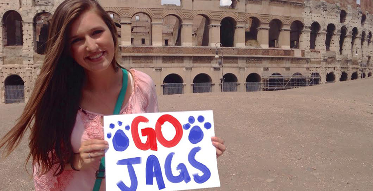 Student holding Go Jags sign while standing in front of Colliseum ruins