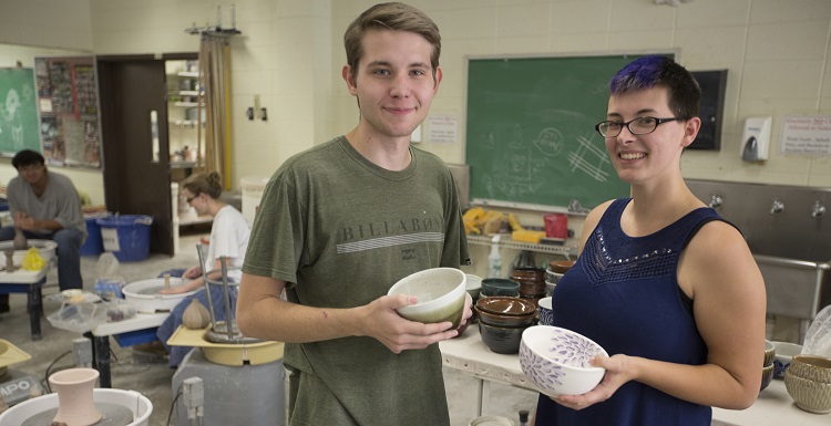 Showing off some of the soup bowls created and donated by USA to benefit Art Soup are Eric Jager, visual arts major, and Alana Kruse, ceramics lab assistant.