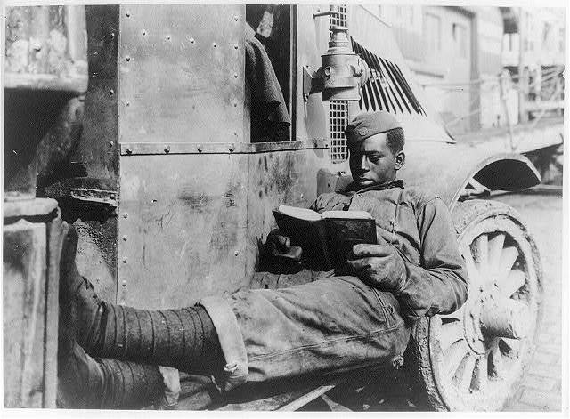 African American soldier at St. Nazaire during the First World War stretched out on the running board of a military vehicle reading a book. Source: Library of Congress archives