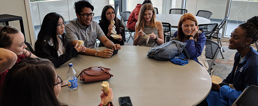 A group of students sitting at a round table talking and eating.