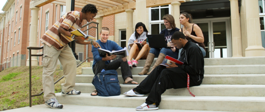 A group of students sitting on steps outside of USA housing with books and laptop.