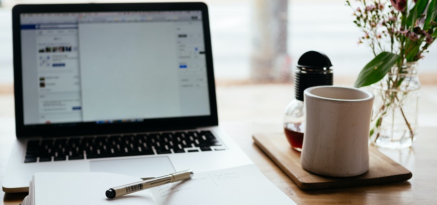 Image of coffee cup on a desk with a laptop, pen and paper